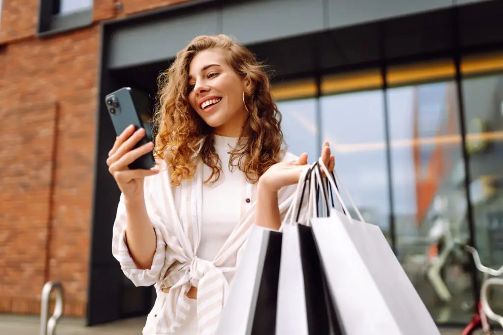Young,Woman,Use,Of,Mobile,Phone,And,Hold,With,Shopping